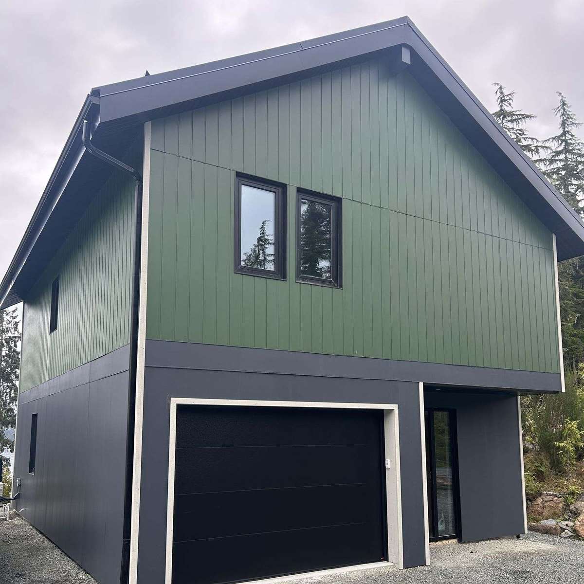 A completed modular home: two storeys with green vertical siding over a charcoal garage level